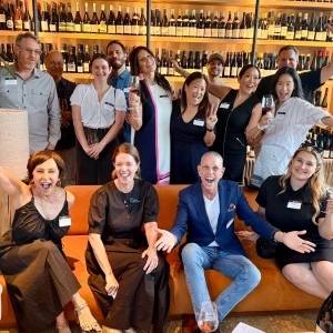 A joyful group of people gathered at a wine event, celebrating local cuisine while holding glasses and smiling.