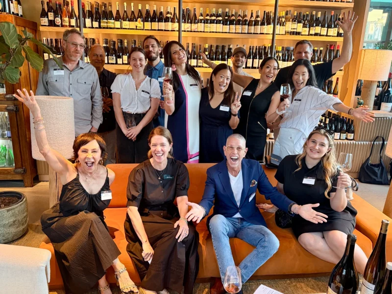 A joyful group of people gathered at a wine event, celebrating local cuisine while holding glasses and smiling.