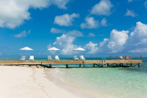 Sun loungers with umbrellas on a wooden pier overlooking the clear turquoise waters and sandy beach in Turks and Caicos.