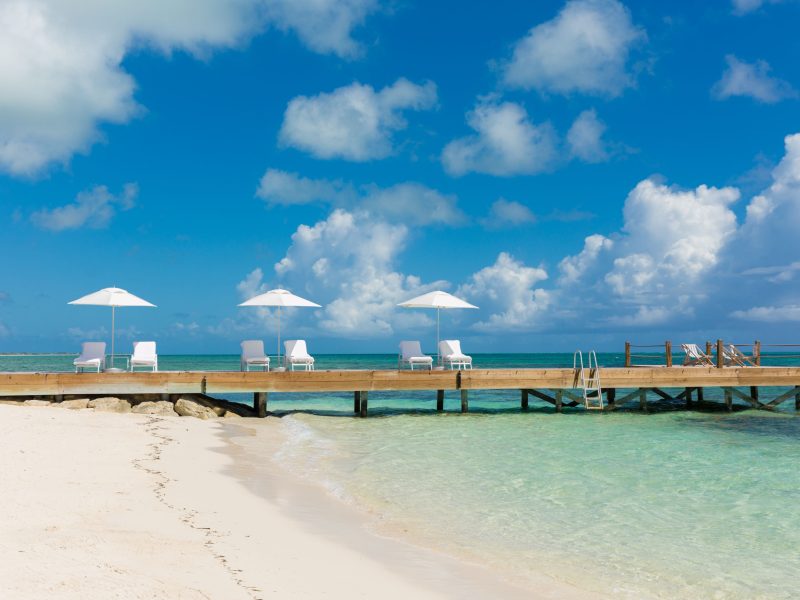 Sun loungers with umbrellas on a wooden pier overlooking the clear turquoise waters and sandy beach in Turks and Caicos.