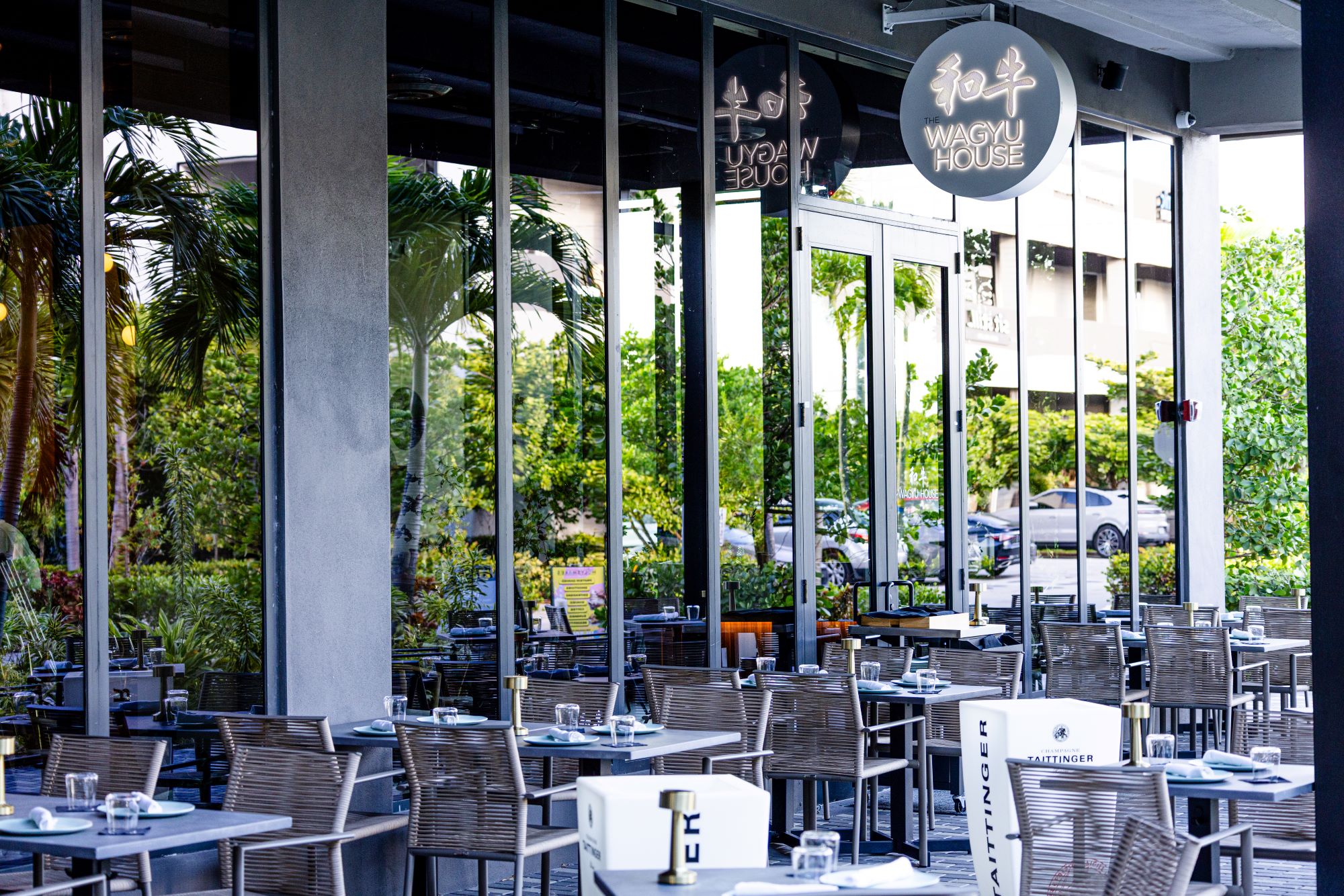 Dining area of The Wagyu House featuring modern decor, outdoor seating, and reflections of greenery and surroundings.