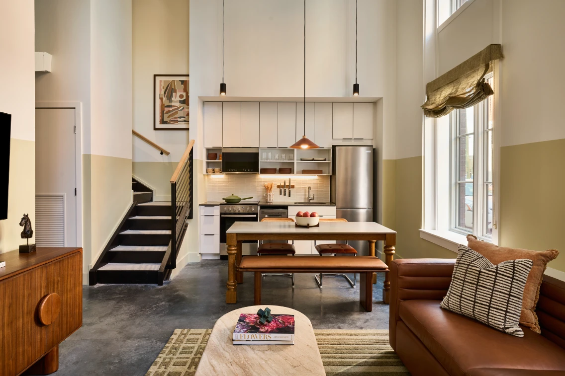 Modern kitchen and dining area featuring a wooden table, leather sofa, and stairs, showcasing an inviting atmosphere in Savannah.
