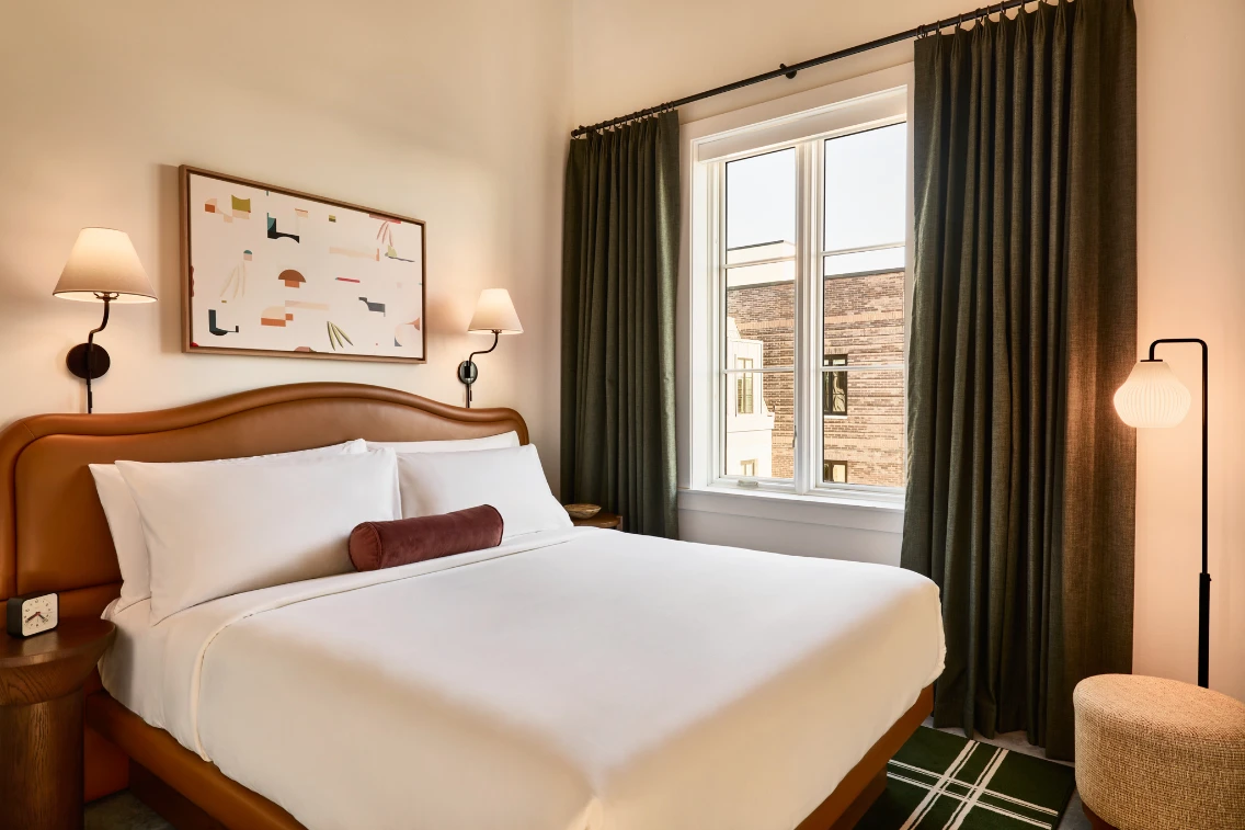 Elegant hotel room featuring a cozy bed, modern decor, and large windows with natural light. Perfect for a relaxing stay.