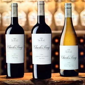 Three bottles of Charles Krug wine, including Merlot, Cabernet Sauvignon, and Chardonnay, displayed on a wooden surface.