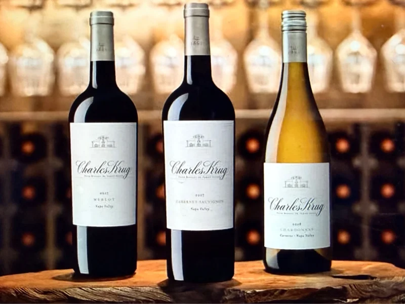 Three bottles of Charles Krug wine, including Merlot, Cabernet Sauvignon, and Chardonnay, displayed on a wooden surface.
