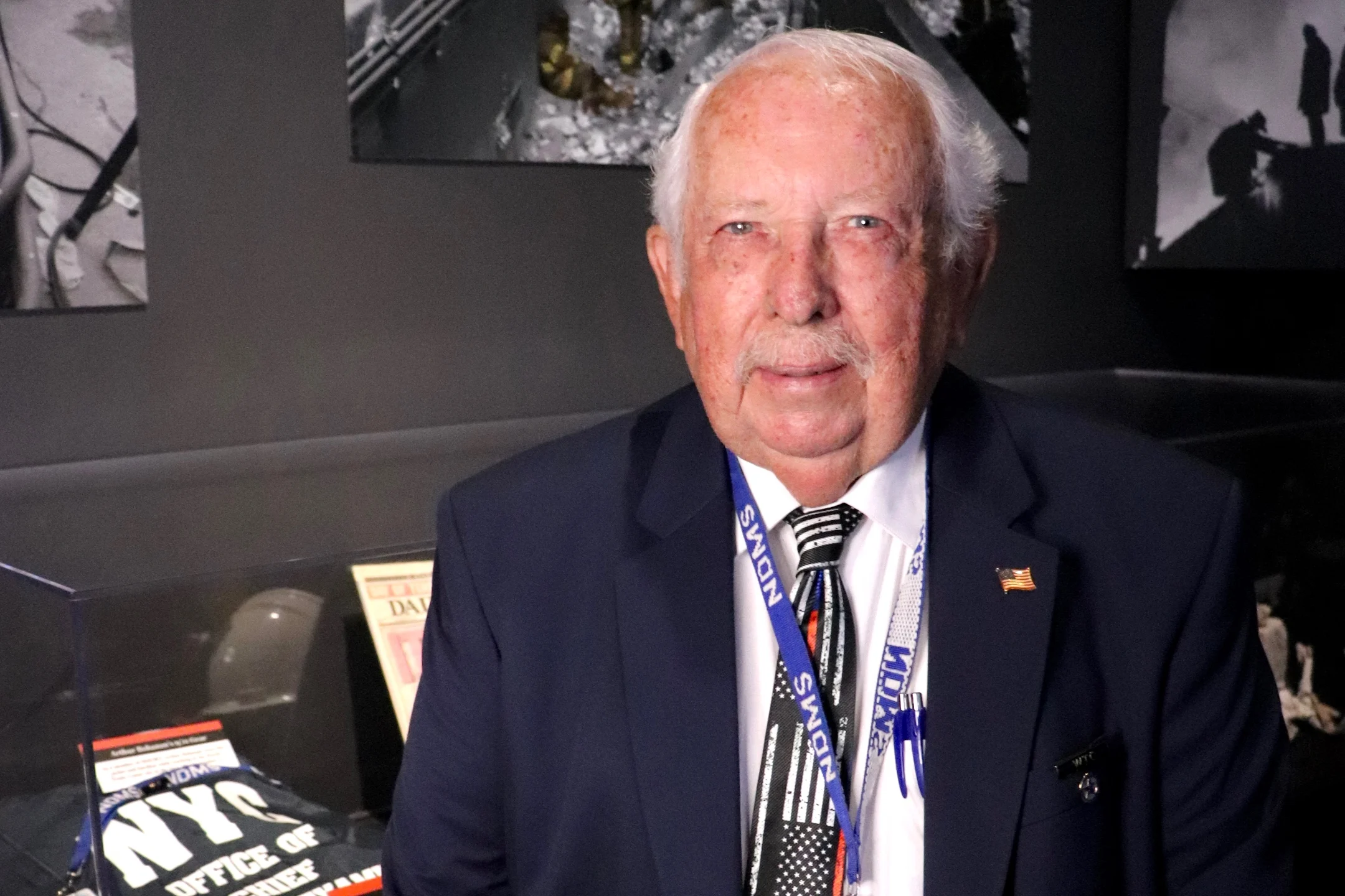 A man in a suit with a tie stands in front of a display, commemorating the 25th anniversary of the 9/11 attack.