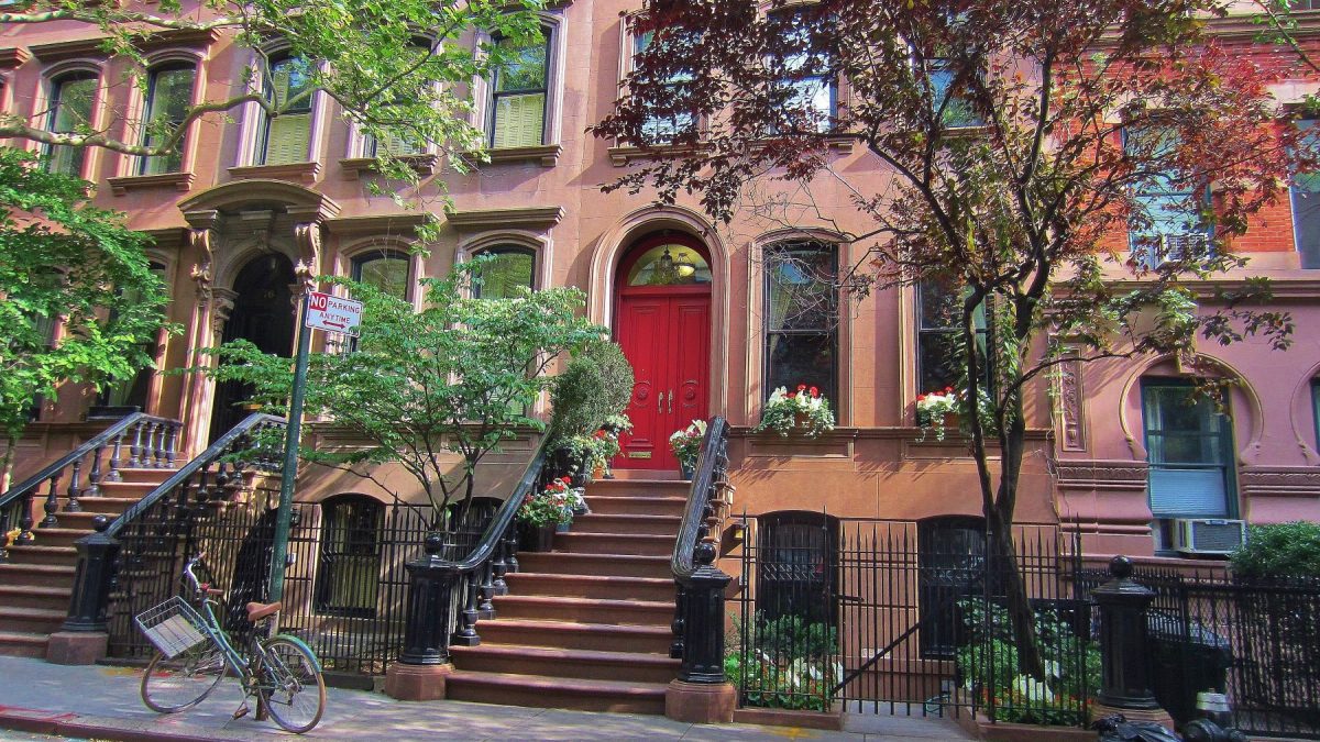 Brownstone building with a red door, surrounded by greenery and a bike parked outside on the Upper West Side of Manhattan.