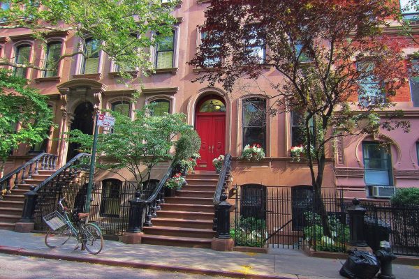 Brownstone building with a red door, surrounded by greenery and a bike parked outside on the Upper West Side of Manhattan.