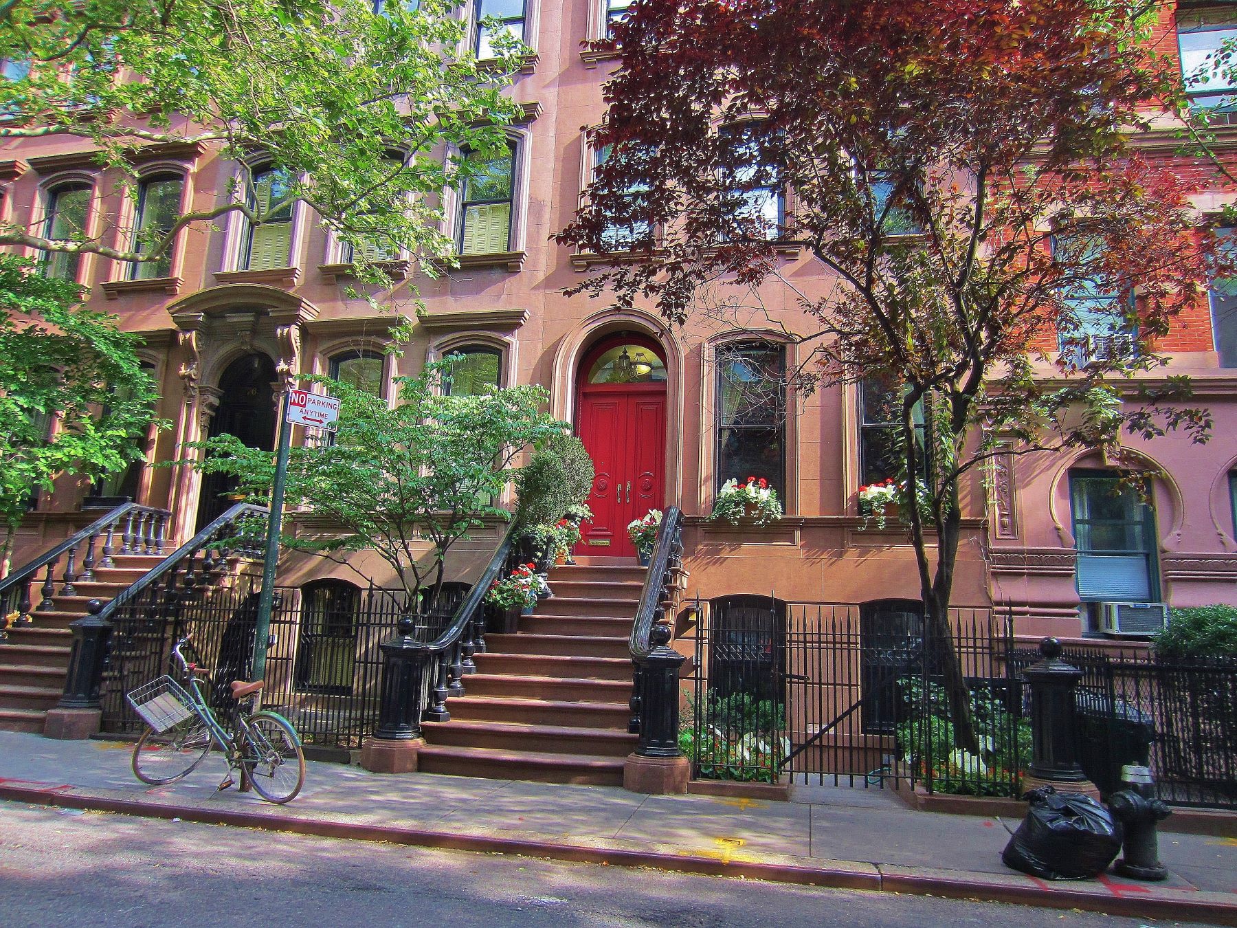 Brownstone building with a red door, surrounded by greenery and a bike parked outside on the Upper West Side of Manhattan.