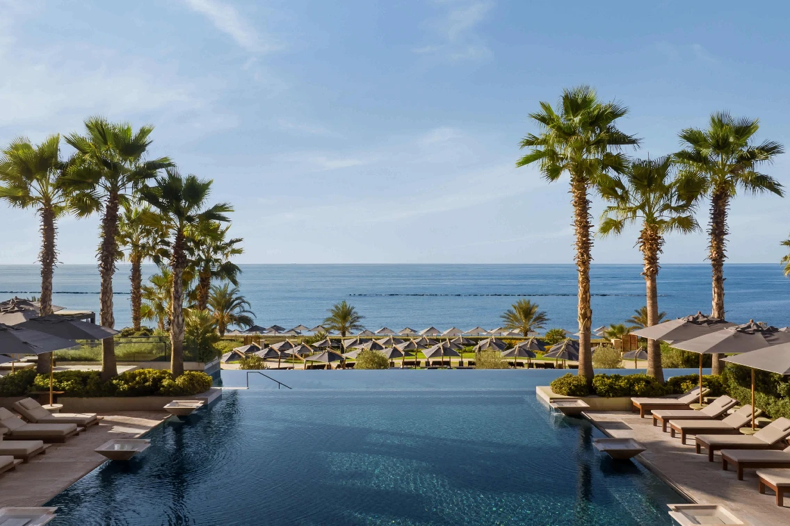 Partial view of the AMARA Hotel's infinity pool, flanked by palm trees, overlooking the Mediterranean Sea and lounge area.