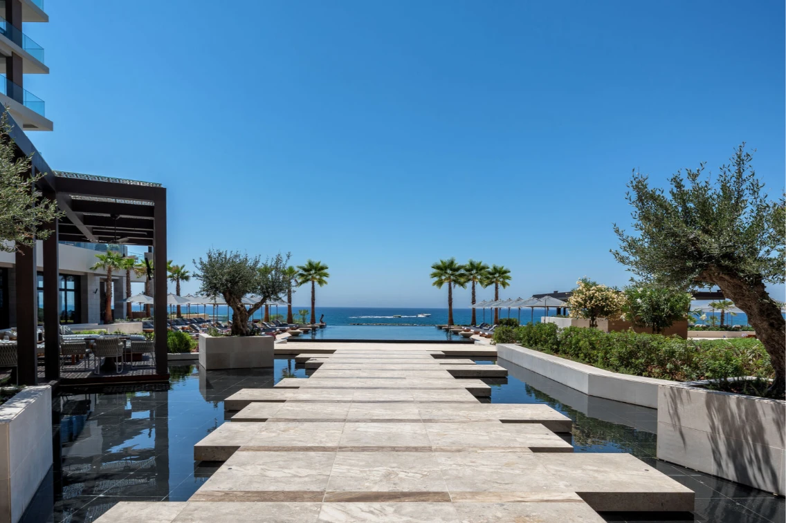 Modern pathways lead to the sea at the AMARA Hotel, surrounded by palm trees and lush landscaping under a clear blue sky.