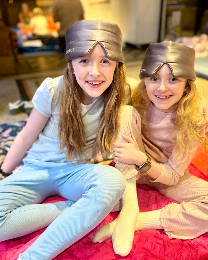 Two girls in pajamas wear matching sleeping caps while sitting on a colorful mat during a sleepover event at a museum.