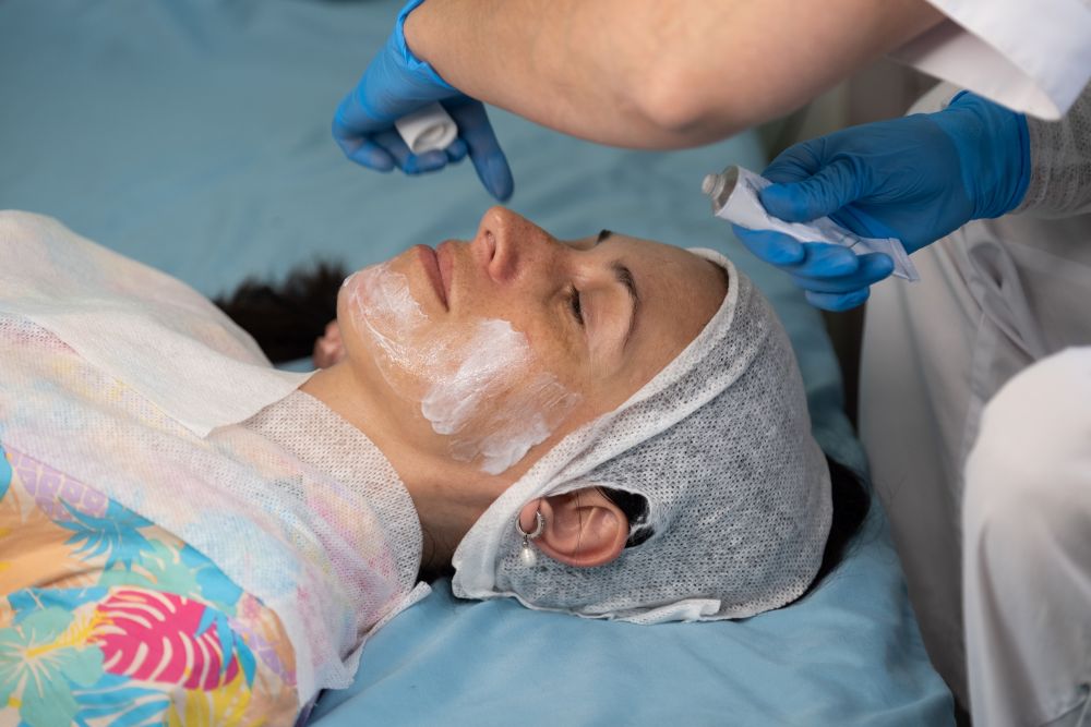 A woman receives a facial treatment while lying on a massage table in a professional aesthetic setting.