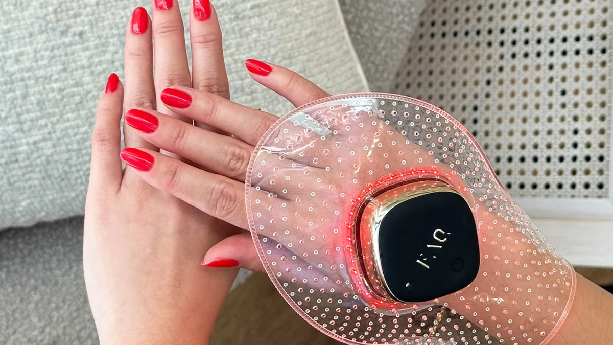 Hands with red nail polish using a FOREO hand care device, featuring a sleek design and glowing red lights in a cozy setting.