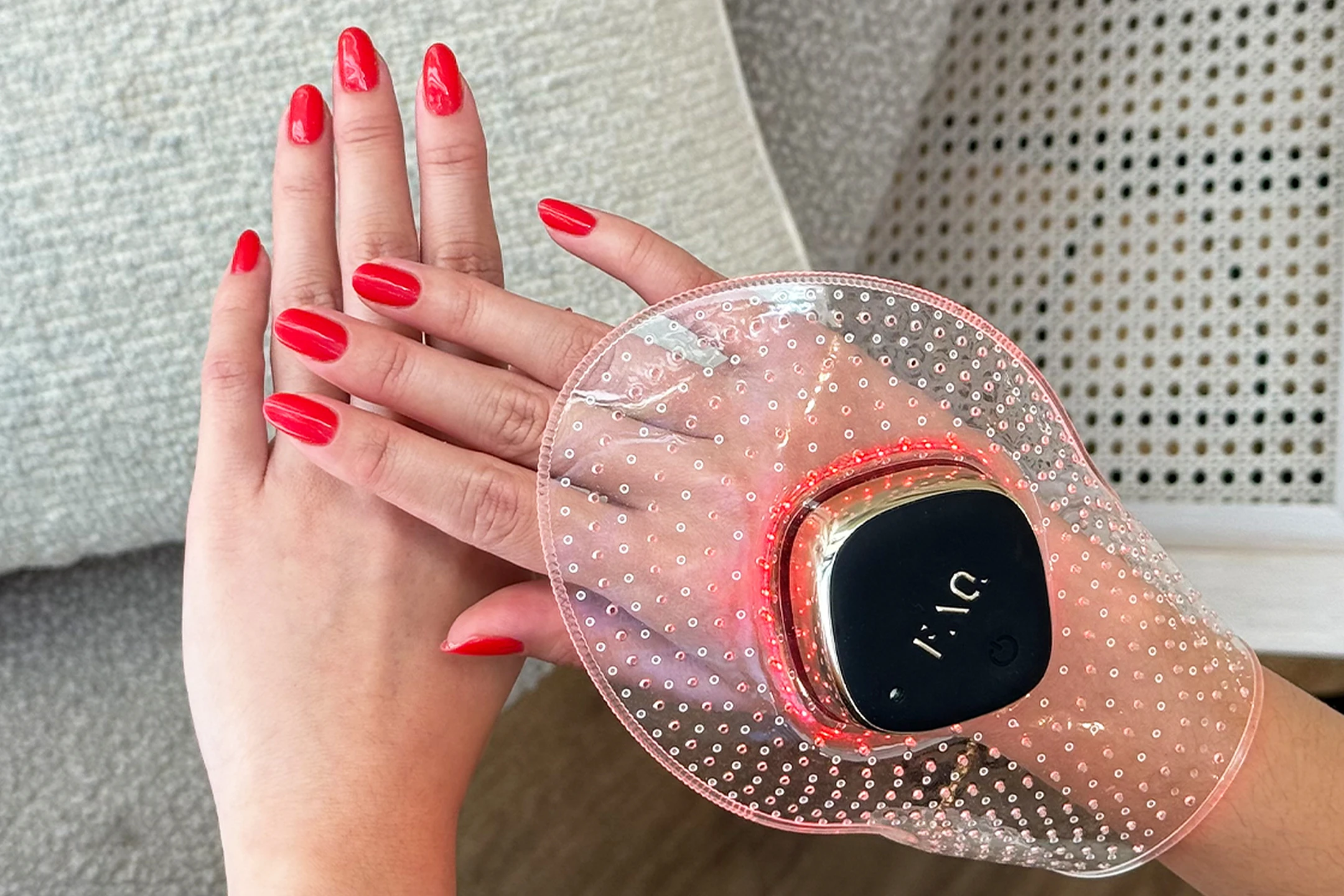 Hands with red nail polish using a FOREO hand care device, featuring a sleek design and glowing red lights in a cozy setting.
