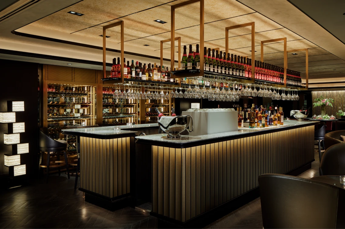 Sophisticated bar with a wide selection of spirits and elegant glassware, illuminated by soft lighting in a luxurious setting.