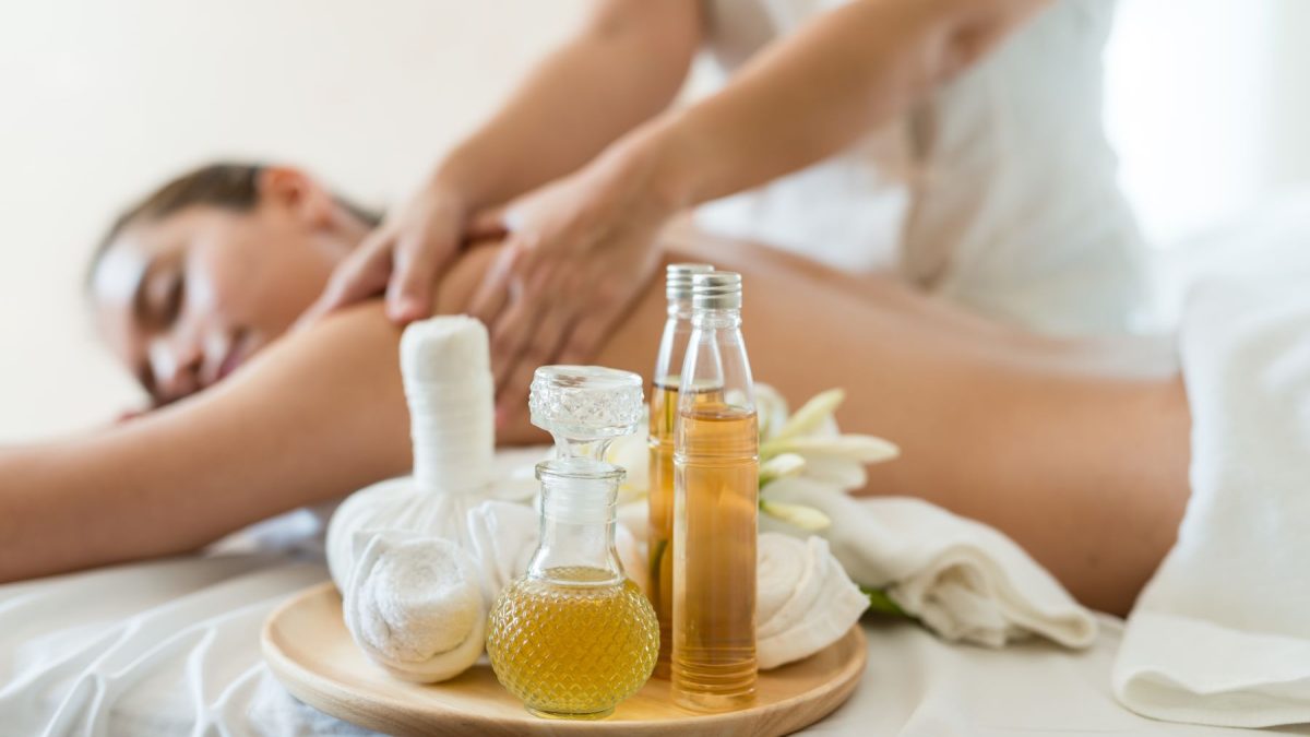 A person receiving a massage with essential oils and soothing items arranged on a tray nearby.