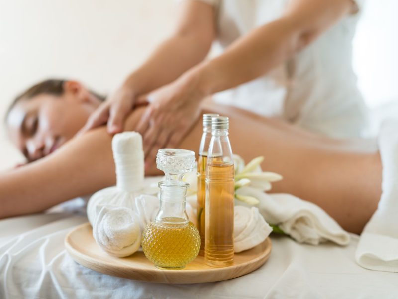 A person receiving a massage with essential oils and soothing items arranged on a tray nearby.