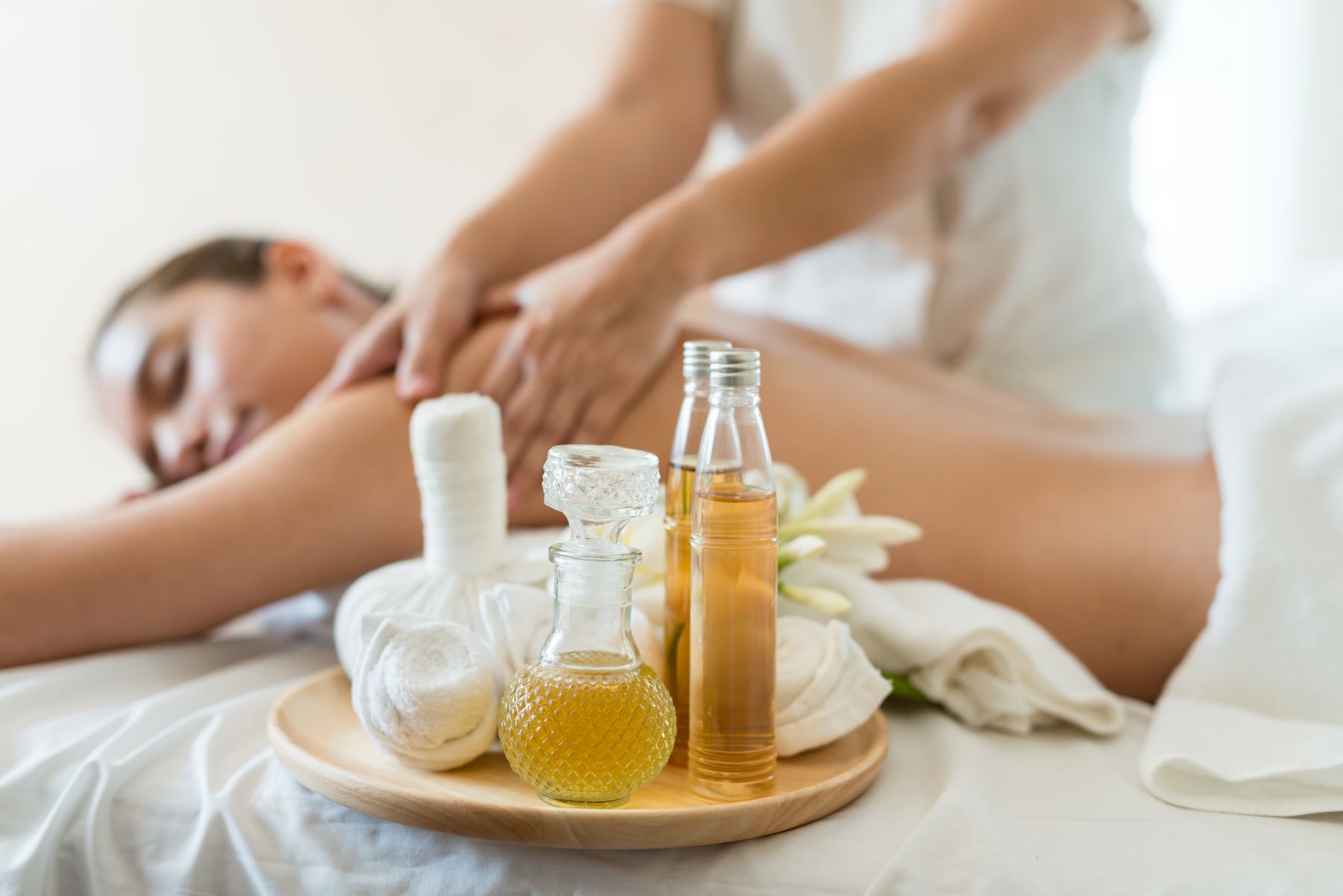A person receiving a massage with essential oils and soothing items arranged on a tray nearby.