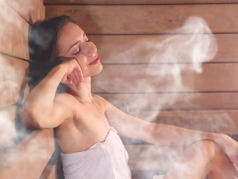 A woman relaxes in a home sauna, surrounded by steam, enjoying a moment of tranquility and warmth.