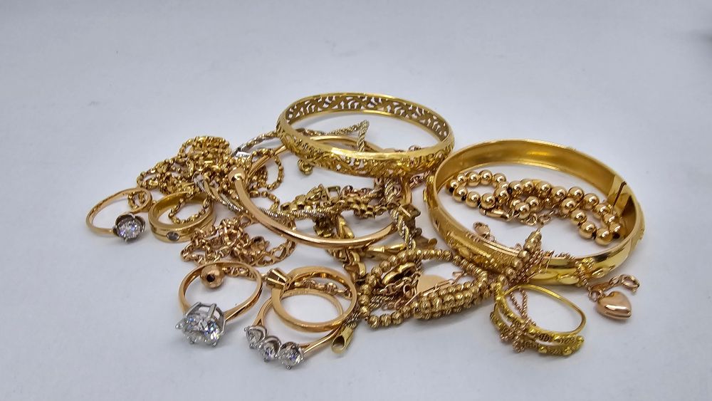 A collection of various gold jewelry pieces, including rings, bangles, and chains, arranged attractively on a white surface.