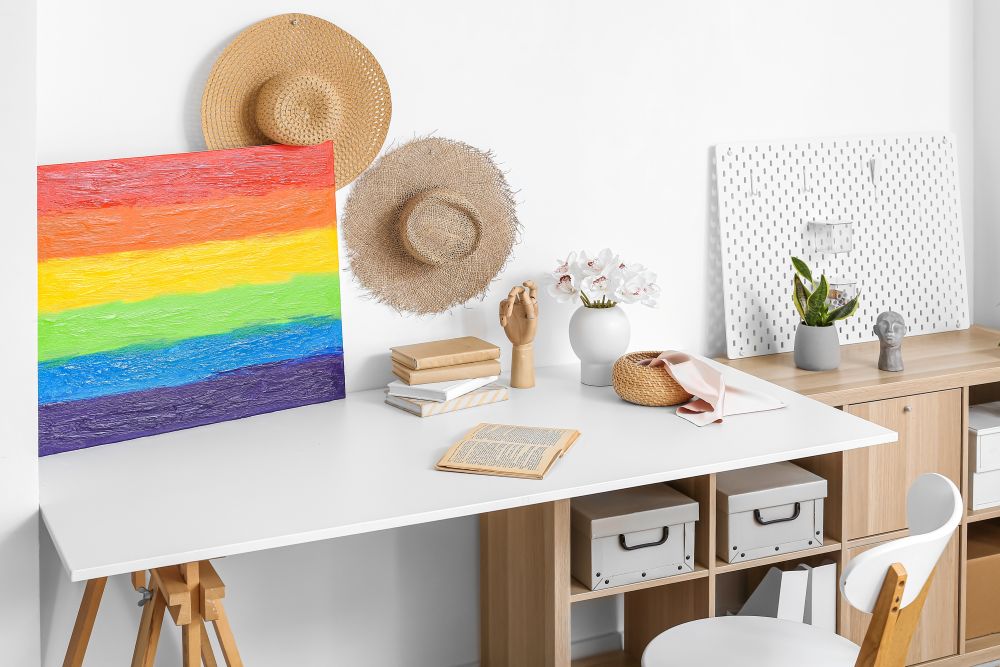 Colorful abstract artwork alongside decorative hats and plants on a modern desk, showcasing a stylish collector's workspace.