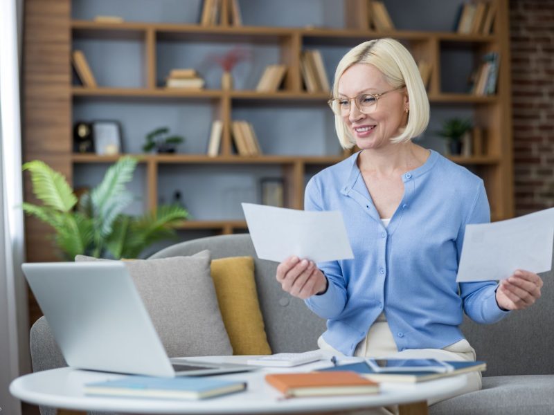 A woman reviews estate planning documents while sitting at a table with a laptop and books in a cozy home office.