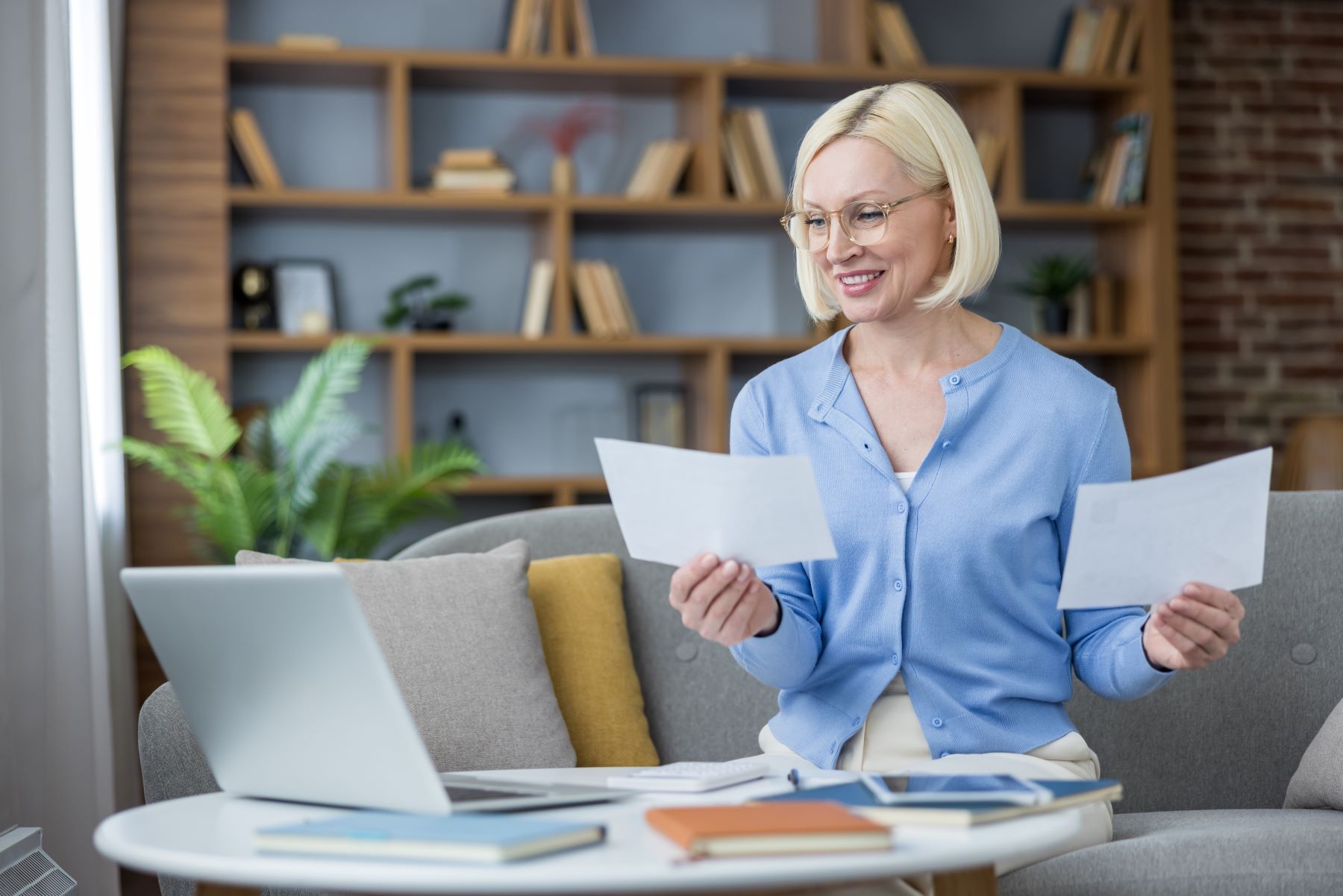 A woman reviews estate planning documents while sitting at a table with a laptop and books in a cozy home office.