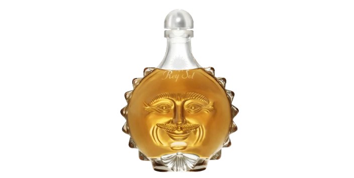A decorative tequila bottle shaped like a sun, featuring a smiling face and filled with amber liquid.