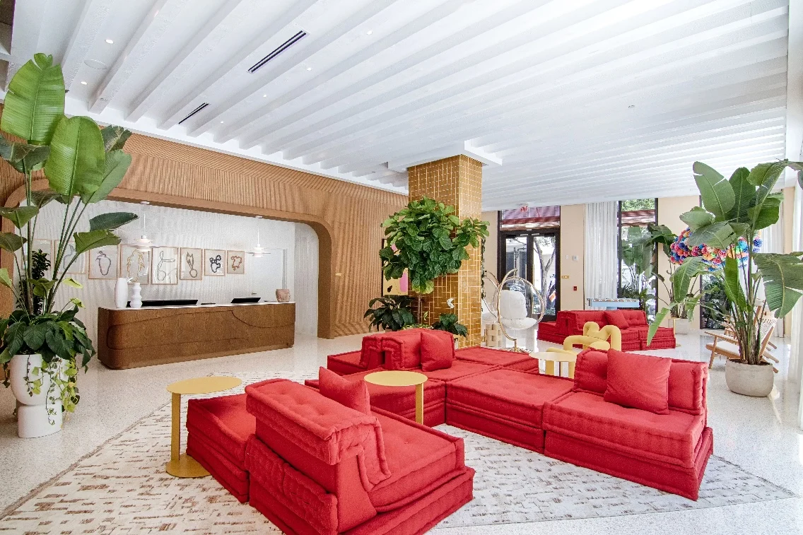 Stylish lounge area with red sofas, tropical plants, and a wooden reception desk in a chic Miami setting.