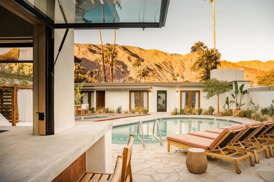 Modern outdoor space featuring a pool, lounge chairs, and palm trees, with mountains in the background in Palm Springs.