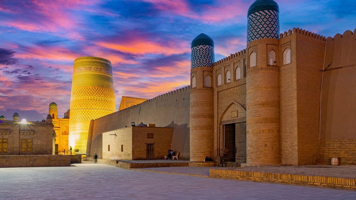 Historic architecture of Uzbekistan under a colorful sunset sky, featuring the iconic Kalta Minor minaret and ancient walls.