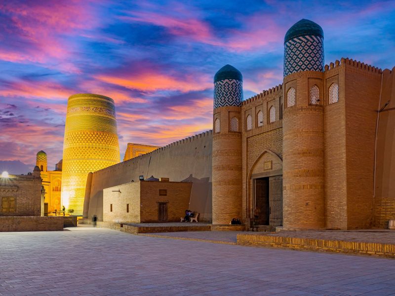Historic architecture of Uzbekistan under a colorful sunset sky, featuring the iconic Kalta Minor minaret and ancient walls.