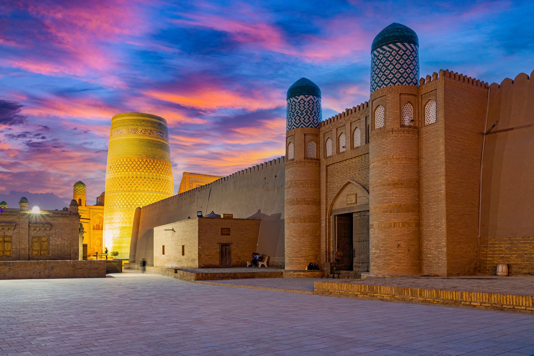 Historic architecture of Uzbekistan under a colorful sunset sky, featuring the iconic Kalta Minor minaret and ancient walls.