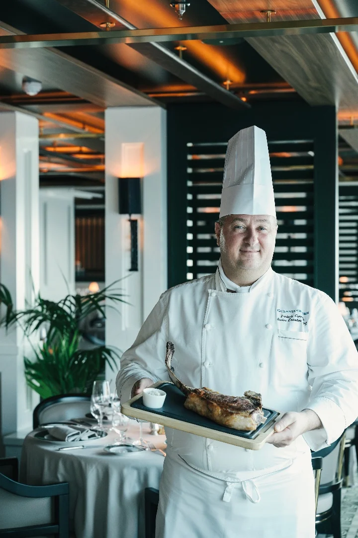 Chef proudly presents a beautifully cooked dish in an elegant restaurant setting, highlighting the gluten-free dining experience.