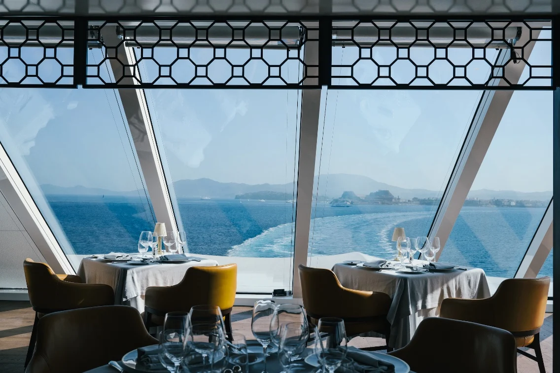 Elegant dining setting with ocean views and mountains in the background, showcasing the relaxing ambiance of a cruise.