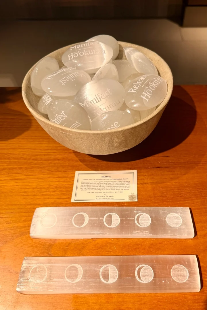 Selenite stones inscribed with words like "Manifest" and "Release" arranged in a bowl, with moon phase carvings below.
