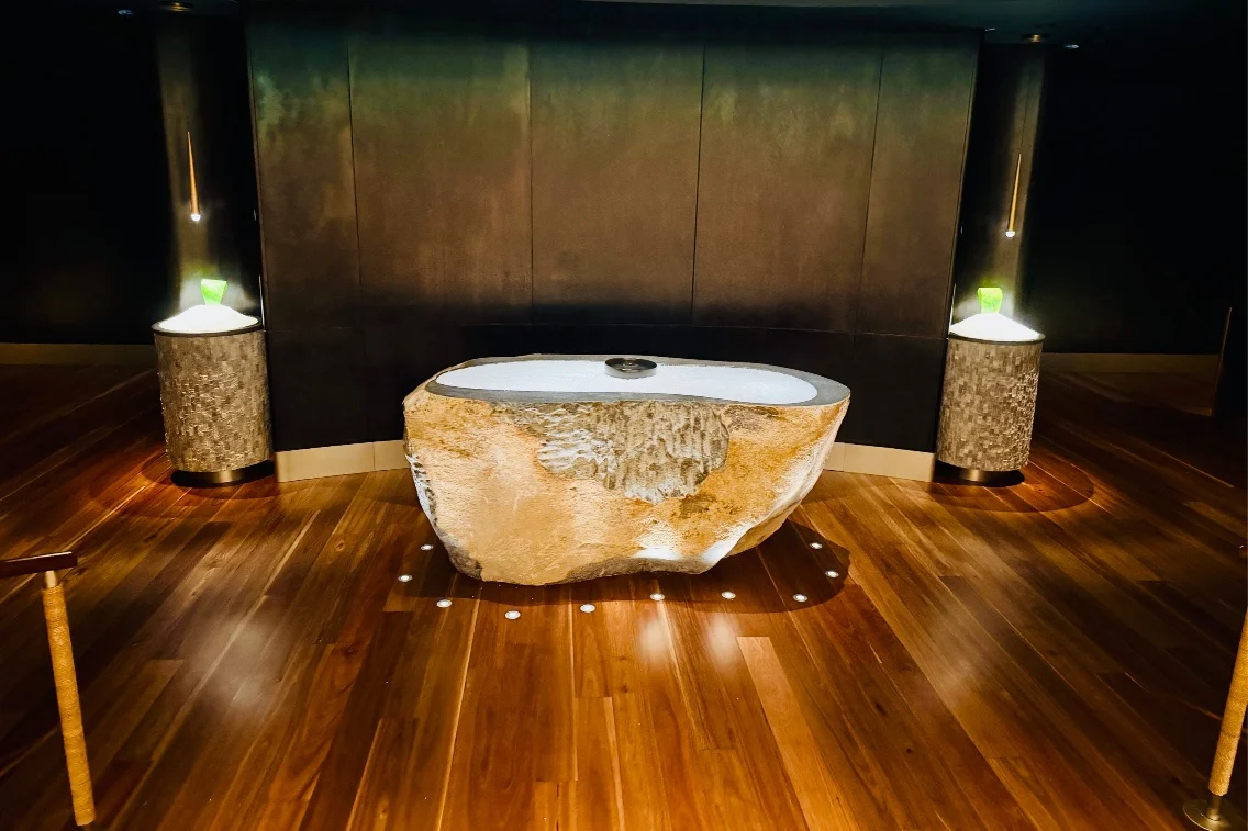Natural stone basin surrounded by wooden flooring and soft lighting, creating a serene spa atmosphere.