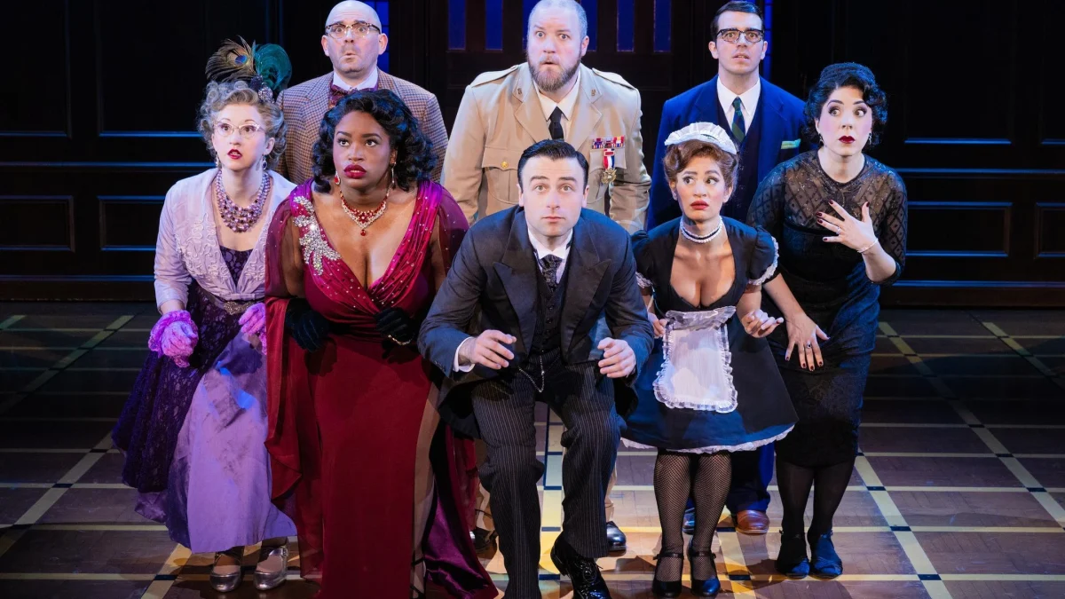 Cast members perform a dramatic scene in 'Clue' on stage, showcasing a mix of surprise and intrigue.