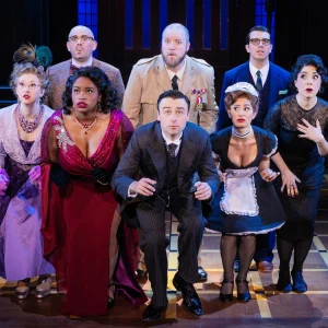 Cast members perform a dramatic scene in 'Clue' on stage, showcasing a mix of surprise and intrigue.