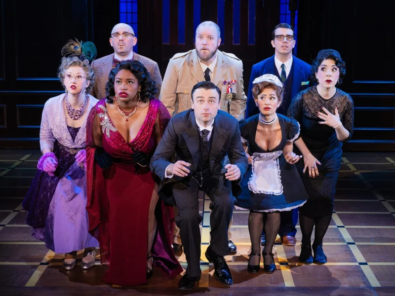 Cast members perform a dramatic scene in 'Clue' on stage, showcasing a mix of surprise and intrigue.