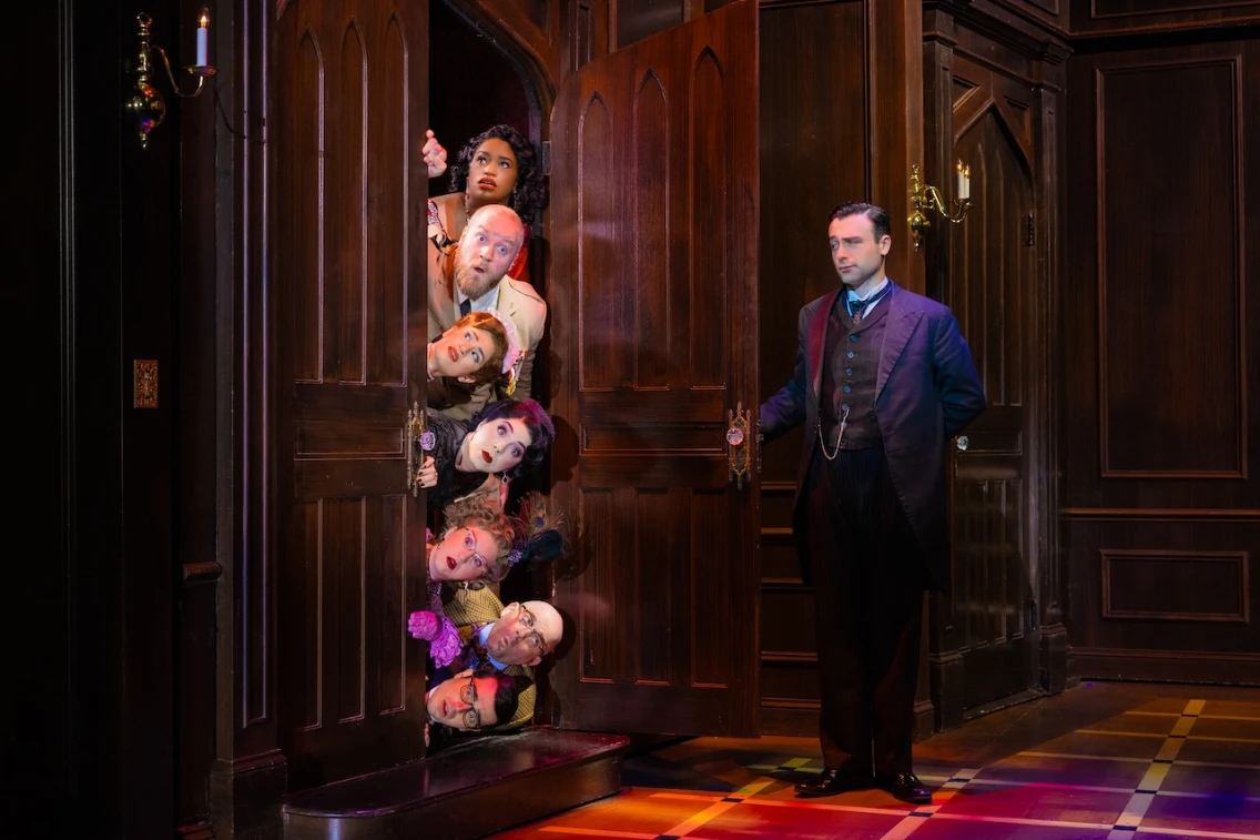 A group of characters peeks through a door while a man in formal attire stands nearby, setting a comedic scene for 'Clue.'