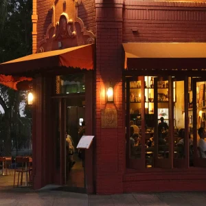 The exterior of First Of All restaurant at night, featuring warm lighting and patrons enjoying their dining experience inside.