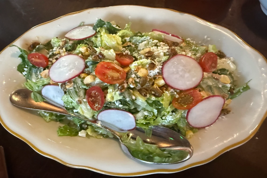 A fresh salad topped with cherry tomatoes, radishes, and crunchy seeds, served in a decorative dish with a spoon.