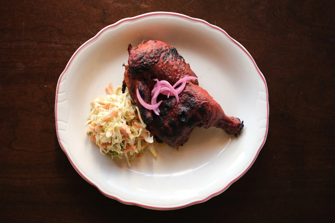 Yucatecan grilled chicken leg served with coleslaw and topped with pickled onions on an oval plate.
