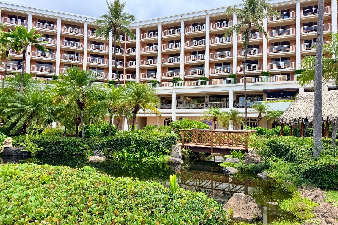 Tropical landscape with palm trees and a wooden bridge leading over a pond, set against the backdrop of the Grand Wailea resort.