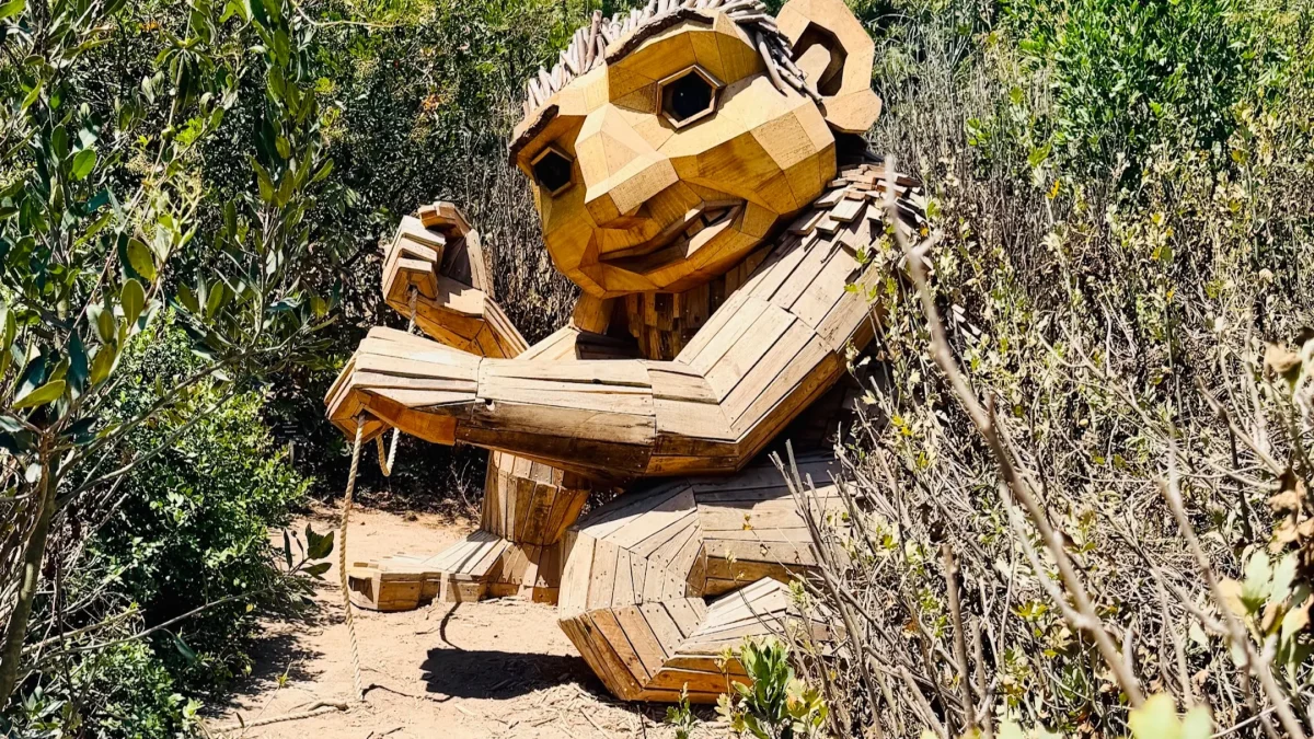 Wooden troll sculpture by Thomas Dambo surrounded by greenery in an outdoor setting.