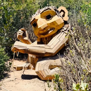 Wooden troll sculpture by Thomas Dambo surrounded by greenery in an outdoor setting.