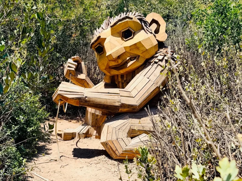 Wooden troll sculpture by Thomas Dambo surrounded by greenery in an outdoor setting.