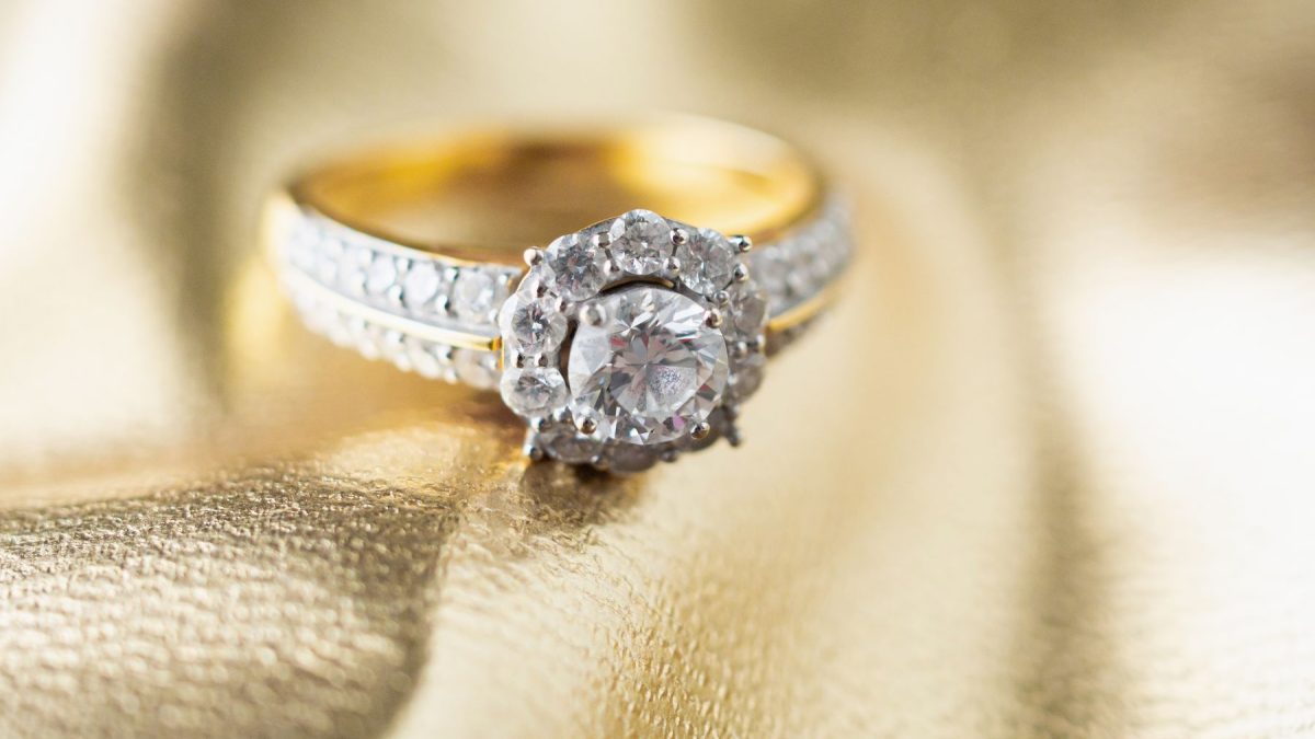 Custom engagement ring featuring a central diamond surrounded by smaller stones on a gold band against a golden background.